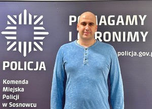 Zdjęcie przedstawia spiranta Tomasza Obwiosło na tle napisu &quot;Komenda Miejska Policji w Sosnowcu Policja Pomagamy i chronimy&quot;.