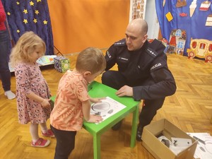 Zdjęcie przedstawia umundurowanego policjanta siedzącego przy stoliku z dziećmi.