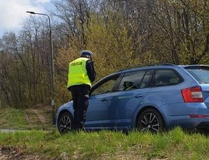 Zdjęcie przedstawia umundurowanego policjanta z wydziału ruchu drogowego stojącego przy niebieskim samochodzie.